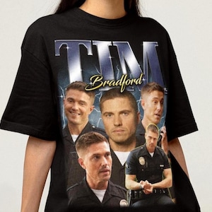 May include: A black short-sleeve t-shirt featuring a graphic print of the character Tim Bradford in various poses. The design includes the name TIM in large metallic-style lettering at the top, the name Bradford in yellow script, and a blue lightning background.