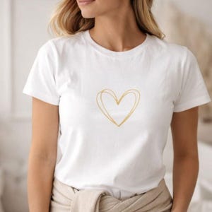 Könnte beinhalten: Weißes T-Shirt mit goldenem Herzdesign. Das kurzärmlige Oberteil hat einen Rundhalsausschnitt und einen minimalistischen Stil. Das Herz ist mit zwei überlappenden Linien gezeichnet, was einen zarten Look erzeugt. Das Shirt besteht aus weichem Material.
