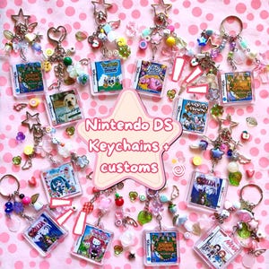 Peut inclure: Une collection de porte-clés en forme de boîtiers de jeux Nintendo DS avec diverses jaquettes, dont Animal Crossing, Nintendogs, Kirby, Harvest Moon, Zelda, Hello Kitty et Nana. Chaque porte-clés est orné de perles colorées et de breloques en étoile.
