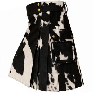 May include: A black and white cowhide kilt with two front pockets and gold-colored button closures. The kilt has a wide black waistband with gold-colored buttons and a buckle closure. The kilt is pleated and has a traditional Scottish design.
