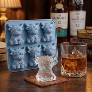 May include: A light blue silicone ice cube tray with six Highland cow shapes. A clear ice sculpture of a Highland cow sits on a brown coaster. A glass of whiskey with a Highland cow ice cube is on the right.