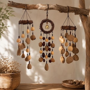 Peut inclure: Trois carillons suspendus à une branche en bois. Chacun présente un cadre circulaire en vigne tressée avec des fils pendants de perles en bois clair, des gousses de graines brunes texturées et des perles sombres polies. Le carillon central inclut une petite cloche en laiton.