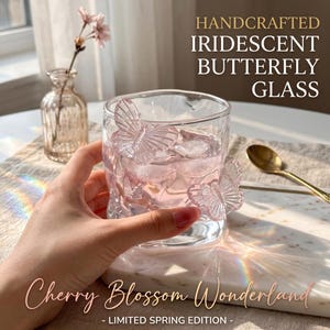 May include: Handcrafted iridescent glass with butterfly accents. The glass is filled with pink liquid and ice. The text on the glass says "Cherry Blossom Wonderland - Limited Spring Edition - ".