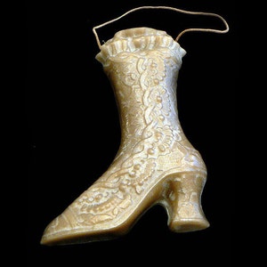 May include: A gold-colored, decorative boot with a high heel and floral pattern. The boot has a small handle at the top and is set against a black background. The boot's design is ornate and detailed.