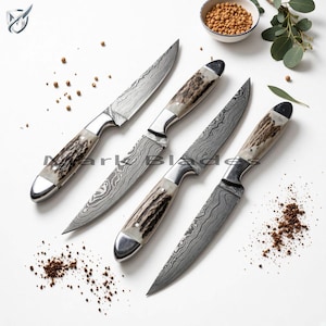 May include: Four knives with Damascus steel blades featuring intricate wavy patterns and textured antler handles with polished metal bolsters. The knives are arranged diagonally on a white surface with scattered brown spices and a small bowl.