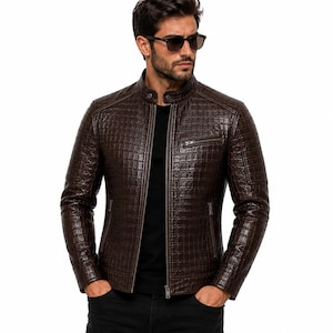 May include: A dark brown leather jacket featuring a textured crocodile-embossed pattern, a stand-up collar with a snap button closure, a front zipper, and a single zippered chest pocket. The jacket has long sleeves and a fitted silhouette.