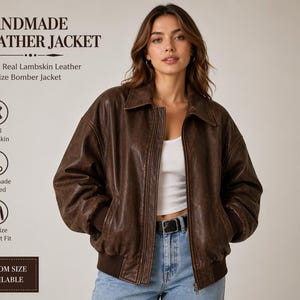 Op de afbeelding: Een bruine, handgemaakte leren bomberjack met kraag en ritssluiting. De jas is gemaakt van 100% echt lamsleer en heeft een oversized pasvorm. De tekst "HANDMADE LEATHER JACKET" staat bovenaan de afbeelding.