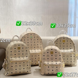 Puede incluir: Cuatro mochilas beige con un patrón repetido de diamantes negros y logotipos. Las mochilas varían en tamaño, la más grande mide 32x39cm y la más pequeña 23x27cm. Cada mochila tiene un asa superior, un bolsillo frontal y herrajes dorados.