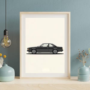 Puede incluir: Impresión enmarcada que presenta una vista lateral de un coupé negro clásico. La obra de arte representa el coche en un estilo minimalista, destacando sus elegantes líneas y diseño. La impresión está enmarcada sobre un fondo crema.