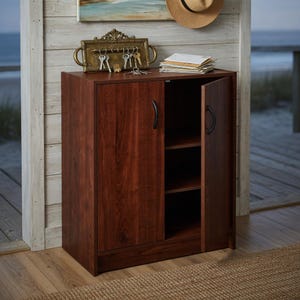 May include: A dark cherry-finished wooden cabinet with two doors, one open to reveal interior shelves. The cabinet has black handles and sits on a wooden floor. A decorative key holder and keys are on top.