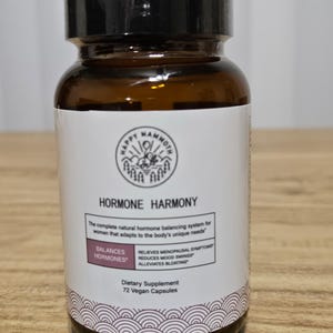 May include: A brown glass bottle with a black cap and a white label. The label reads "HORMONE HARMONY" and lists benefits like balancing hormones and relieving menopausal symptoms. The bottle contains 72 vegan capsules.