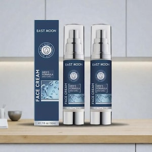 Op de afbeelding: Een display van huidverzorgingsproducten, waaronder twee pompflessen en een doos. De flessen en doos zijn gelabeld met "East Moon Men's Formula Face Cream Daily Care". Elke fles bevat 50 ml. De verpakking is marineblauw.