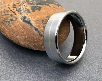 May include: A silver and black wedding band with a brushed finish. The band has a beveled edge and a flat top.