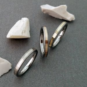 Puede incluir: Tres anillos de plata con una fina banda de oro alrededor del borde. Los anillos est&aacute;n apilados uno encima del otro.