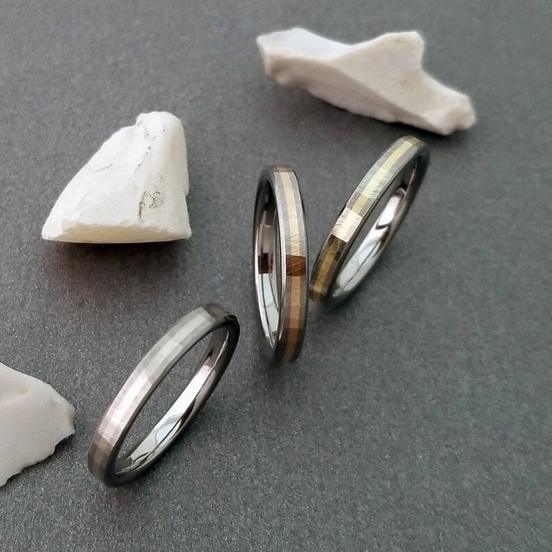 Puede incluir: Tres anillos de plata con una fina banda de oro alrededor del borde. Los anillos est&aacute;n apilados uno encima del otro.