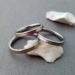 Puede incluir: Tres anillos de plata con finas bandas doradas y de cobre. Los anillos est&aacute;n apilados uno encima del otro y descansan sobre una roca blanca.