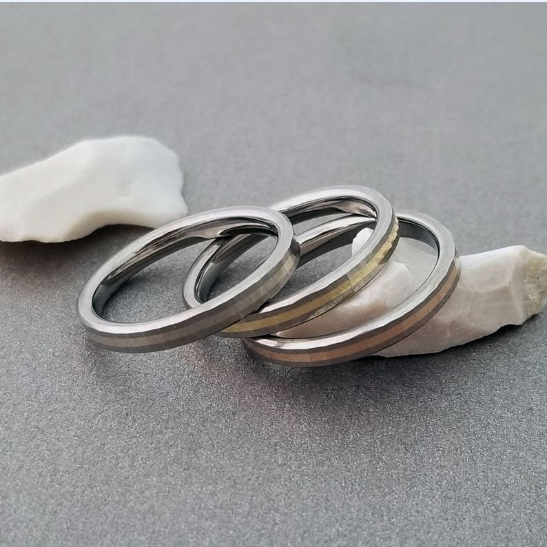 Puede incluir: Tres anillos de plata apilados uno encima del otro. El anillo superior tiene una fina banda dorada alrededor.