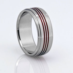 May include: A silver ring with three red lines around the band.