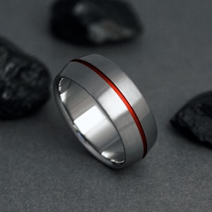May include: A silver wedding band with a red line down the center.