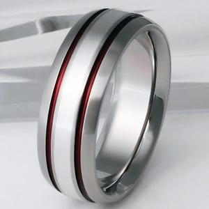 May include: A silver and red titanium ring with a beveled edge and two red lines.