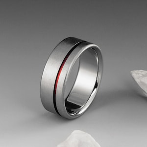 May include: A silver ring with a red line inlay. The ring is brushed and has a polished inner band.