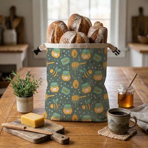 Puede incluir: Una bolsa de pan llena de hogazas de pan, con un diseño de miel. La bolsa está decorada con abejas, tarros de miel y cucharas de miel sobre un fondo verde oscuro. La bolsa está sobre una mesa de madera.