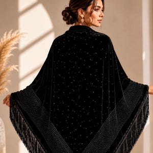 Peut inclure: Un châle en velours noir de forme triangulaire, doté d'une large bordure ornée de strass denses et scintillants, ainsi que de longues franges fluides sur les bords. Le corps du châle est parsemé de petits strass décoratifs.