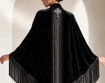 Op de afbeelding: Een zwarte fluwelen cape met een centraal verticaal paneel met een ruitpatroon, versierd met een zilverkleurige kristallen broche bij de halslijn. Het kledingstuk is verfraaid met verspreide strass-steentjes en afgewerkt met lange zwarte franjes.