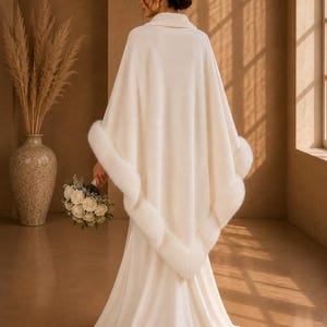 Bride wearing an ivory bridal shawl with faux fur trim viewed from the back, elegant winter wedding wrap paired with a satin wedding gown in a luxury studio.