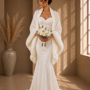 Front portrait of a bride holding white flowers while wearing an ivory bridal wrap with faux fur trim for winter weddings.