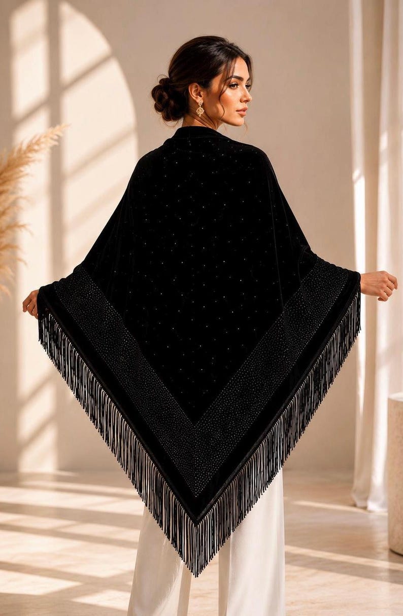 A black velvet triangular shawl featuring a wide border embellished with small sparkling crystals and a long fringe trim along the edges. The fabric is adorned with scattered crystal accents throughout the main body of the garment.