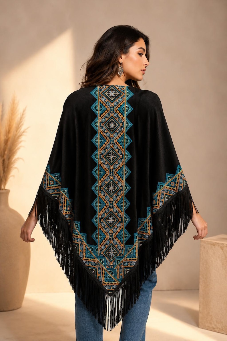 Black shawl with a geometric design in teal, orange, and gold. The poncho has fringe along the bottom and sleeves. The design is centered on the back and along the edges of the sleeves.