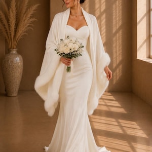 Bride walking in a satin wedding dress wearing an ivory faux fur bridal shawl, elegant winter wedding cover up with soft draped silhouette.