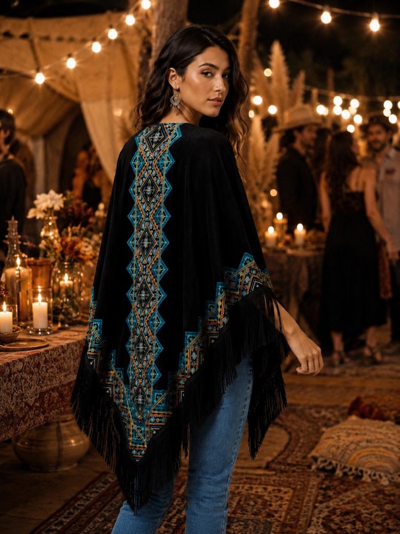 Black velvet shawl with intricate turquoise and orange geometric embroidery. The poncho features long fringe along the bottom edge. The garment is worn over blue jeans.