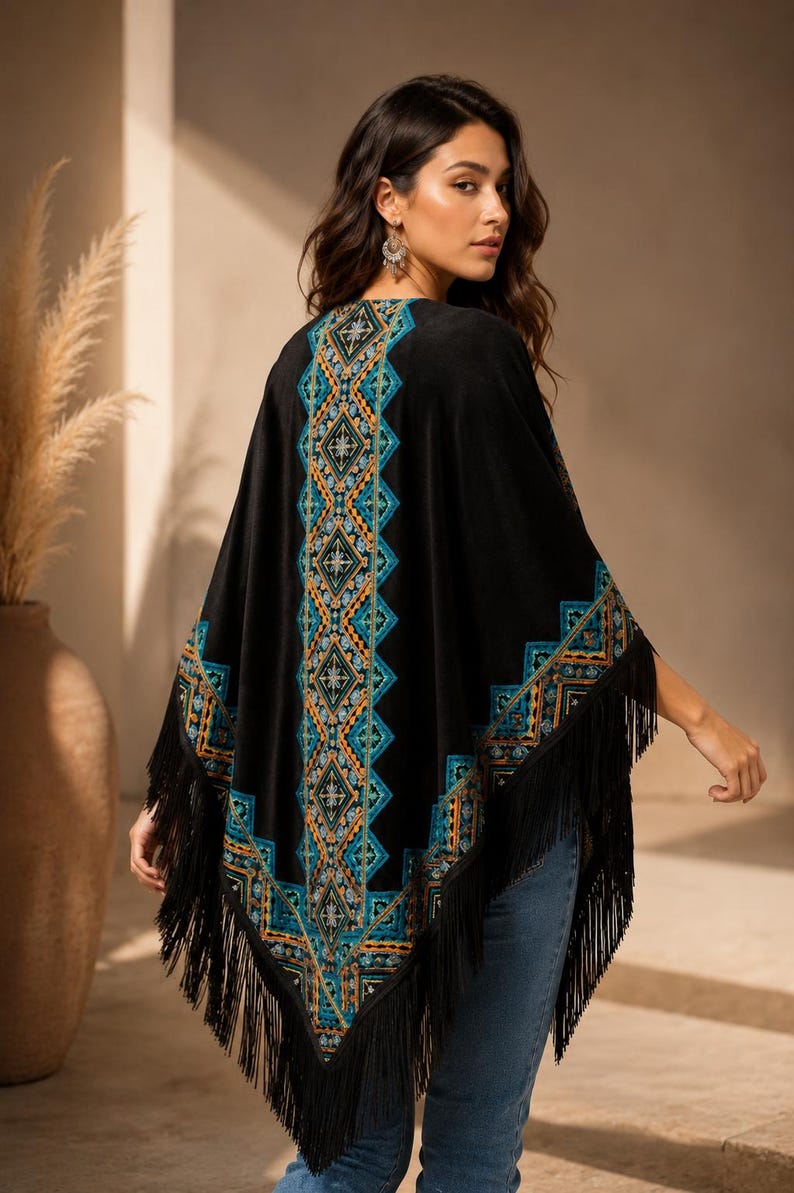 Black shawl with a geometric pattern in teal, orange, and gold. The poncho has a fringe trim along the bottom edge. The model is wearing blue jeans.