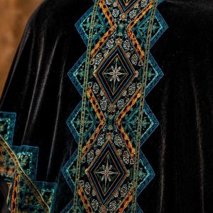 The design features geometric patterns in teal, orange, and gold, creating a striking contrast against the dark fabric. The embroidery is detailed and appears to be hand-stitched, adding to the garment's unique appeal.