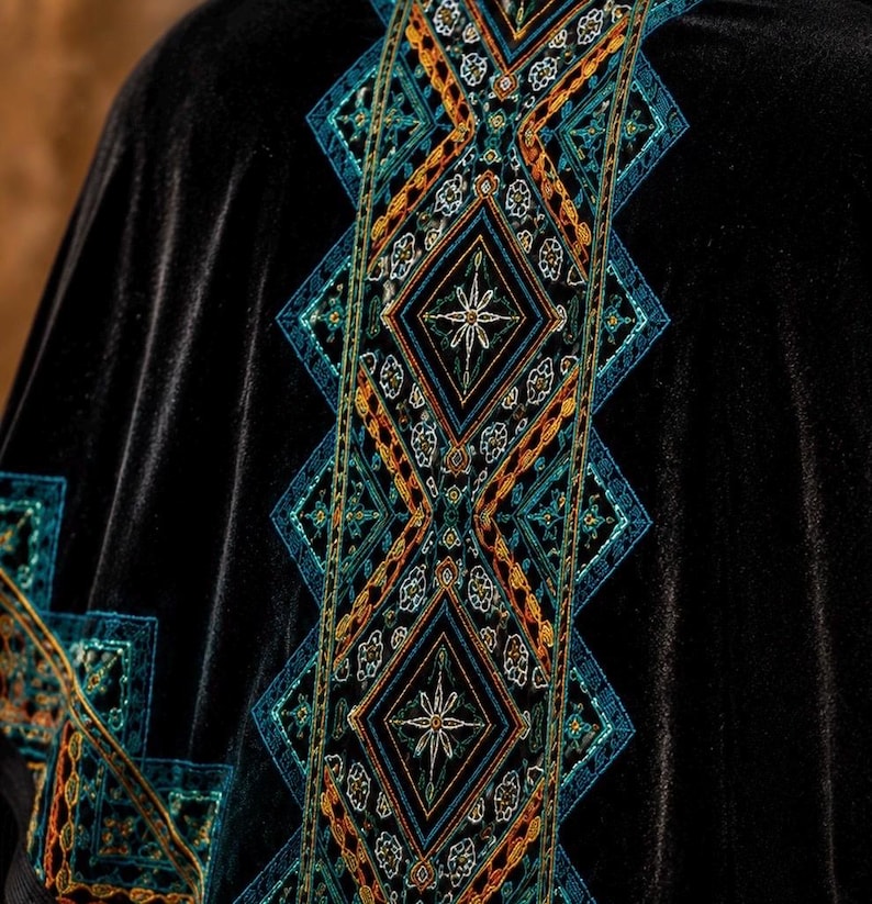 The design features geometric patterns in teal, orange, and gold, creating a striking contrast against the dark fabric. The embroidery is detailed and appears to be hand-stitched, adding to the garment's unique appeal.