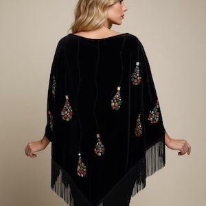 A black velvet poncho featuring a wide boat neckline and long fringe trim along the hem. The garment is decorated with vertical rows of dangling, teardrop-shaped embellishments composed of multicolored, faceted stones and beads.
