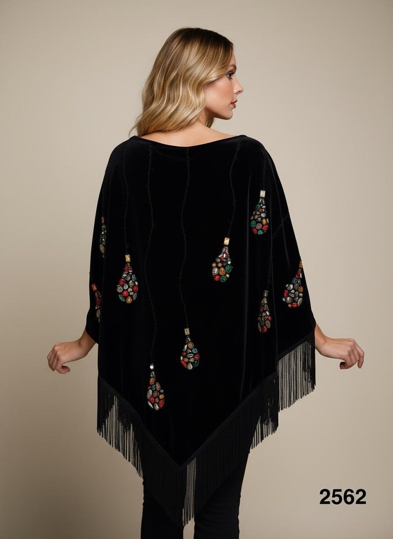A black velvet poncho featuring a wide boat neckline and long fringe trim along the hem. The garment is decorated with vertical rows of dangling, teardrop-shaped embellishments composed of multicolored, faceted stones and beads.