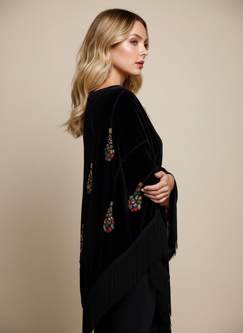 Black velvet shawl with colorful beaded embellishments and fringe trim. The long sleeves and open front create a flowing silhouette. A stylish and elegant garment.