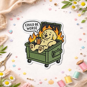 May include: An embroidered patch featuring a light yellow dog sitting inside a green dumpster surrounded by orange and yellow flames. The dog holds a brown coffee cup, and a speech bubble above the dog contains the text COULD BE WORSE.
