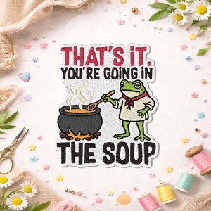 May include: Embroidered patch featuring a green frog in a chef's outfit, holding a wooden spoon over a bubbling cauldron. Text reads "THAT'S IT. YOU'RE GOING IN THE SOUP" in red and black.