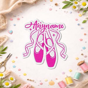 May include: A white embroidered patch featuring a pair of bright pink ballet slippers with long ribbons. The word "Anyname" is stitched in a vibrant pink cursive script above the shoes, surrounded by a white border and small star accents.