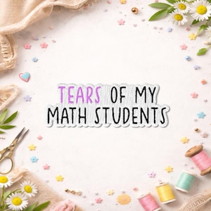 May include: A white sticker with the text "TEARS OF MY MATH STUDENTS" in black and purple. The sticker is surrounded by craft supplies, including spools of thread, scissors, and flowers.