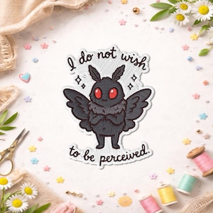 Peut inclure: Un écusson brodé blanc représentant un papillon de nuit gris foncé aux yeux rouge vif, debout les bras croisés. Le texte "I do not wish to be perceived" est inscrit en lettres cursives noires stylisées au-dessus et en dessous.