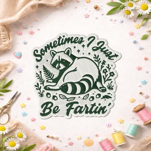 May include: Embroidered patch featuring a raccoon with the text "Sometimes I Just Be Fartin'". The patch is white with dark green embroidery. The raccoon is surrounded by floral and leaf designs. Daisies, sewing supplies, and decorative elements surround the patch.