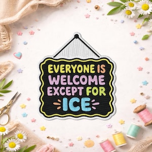 May include: Black sign with yellow trim and the text "EVERYONE IS WELCOME EXCEPT FOR ICE" in colourful embroidered letters. The sign is hanging from a black string. The background includes flowers, spools of thread, and decorative shapes.