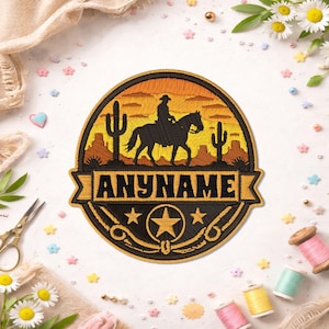 May include: A round embroidered patch featuring a black silhouette of a cowboy riding a horse against a yellow and orange desert sunset background with cacti. Below the scene, a banner displays the text ANYNAME above a star and rope design.