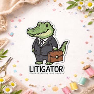 May include: Embroidered patch featuring a green alligator in a suit, holding a briefcase. The patch has the word "LITIGATOR" in bold, black letters. The alligator is smiling. The patch is surrounded by decorative elements.