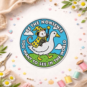 May include: Embroidered patch featuring a possum wizard riding a goose, with the text "Be the nonsense you want to see in the world." The patch has a blue border, green grass, and a whimsical design.